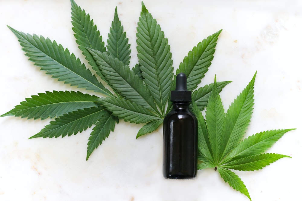 Description: green cannabis leaves and black glass drops bottle